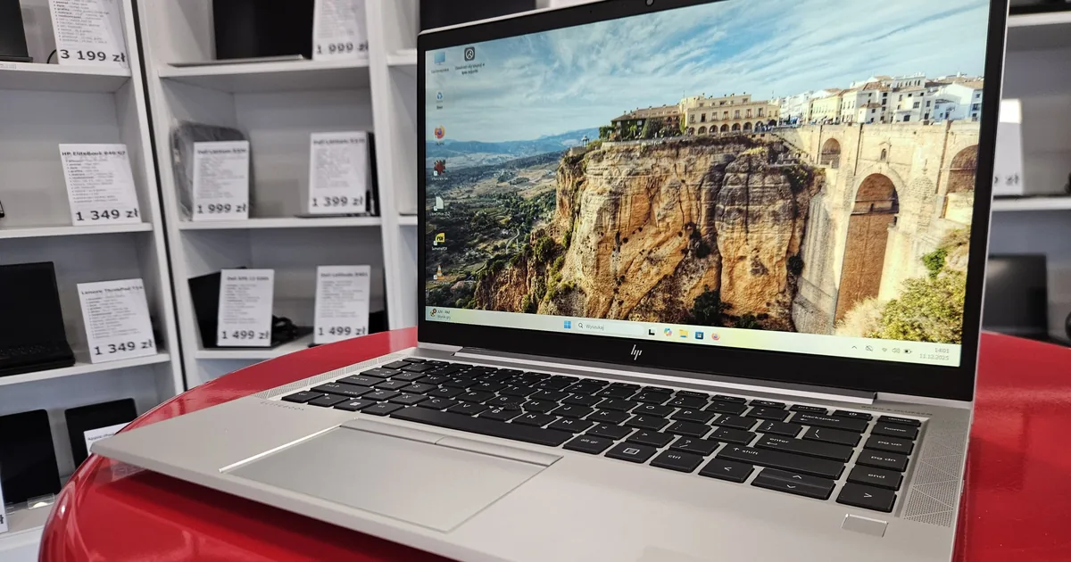 Srebrny HP EliteBook z widocznym logo HP, otwarty na ladzie oddziału; w tle regały z opisanym sprzętem poleasingowym