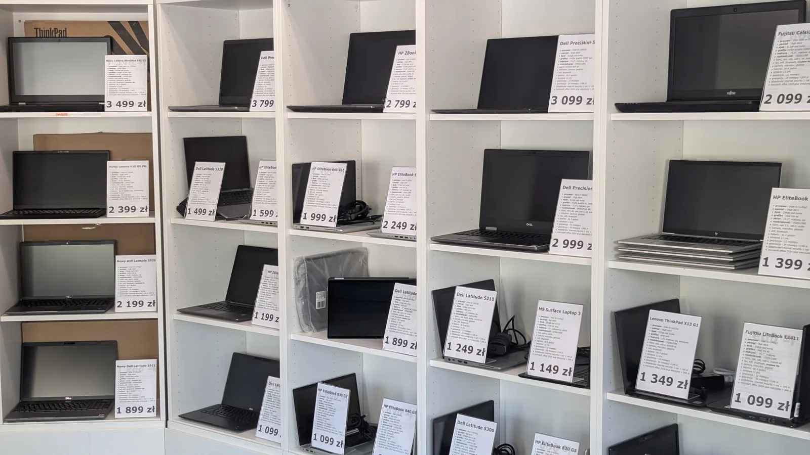 Półki z laptopami poleasingowymi i metkami cenowymi w sklepie w Pruszkowie