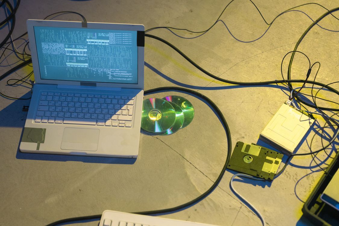 Laptop otoczony kablami i płytami CD — wizualizacja drugiego życia sprzętu elektronicznego i korzyści środowiskowych refurbishingu
